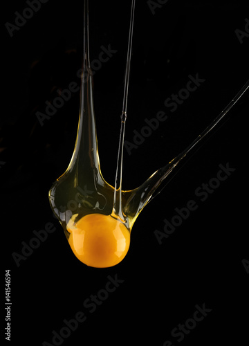 Egg yolk dripping, falling on black background.