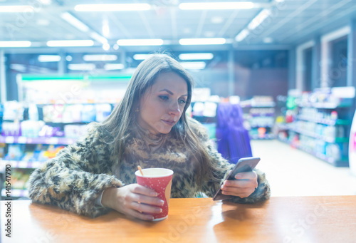 Woman using app on smartphone and drinking coffee in cafe