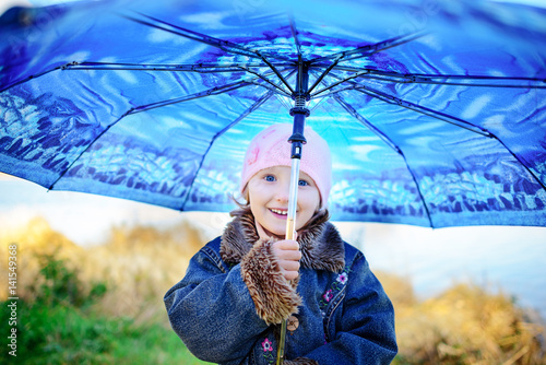 Little girl and boy with umbrella playing in the rain. Kids play outdoor by rainy weather in fall. Autumn fun for children. Toddler kid in raincoat and boots walk in the garden. photo