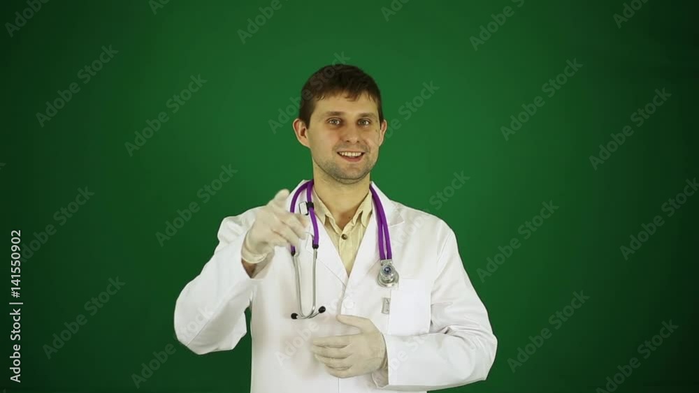 The doctor points a finger at the camera. A male doctor on a green background. Positive young doctor. The doctor points a finger at the camera. A male doctor on a green background. Positive young doctor.