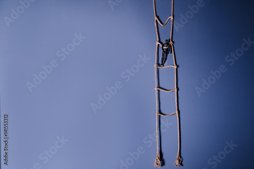 Canvas Print Wooden dark mannequin standing on the hanging rope ladder on the blue background