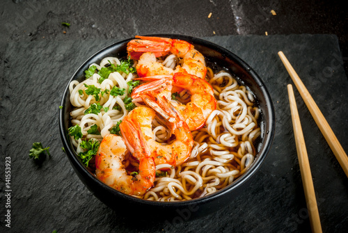 Asian soup with noodles (ramen), with miso paste, soy sauce, greens and shrimps prawn. On a black stone table, with chopsticks. Copy space