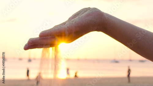 Close up view of sea sand running through a womans hands against a blurred ocean with rest people conceptual of a summer vacation photo