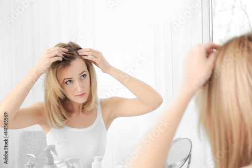 Fototapeta Naklejka Na Ścianę i Meble -  Young woman with hair loss problem looking in mirror at home