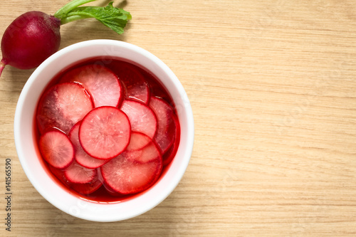 Fresh radishes cut in thin slices pickled in red wine vinegar with sugar and salt, photographed overhead with natural light (Selective Focus, Focus on the radish slices on the top)