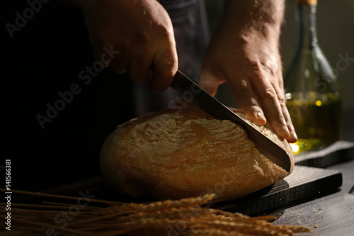 Man cutting bread on kitchen table, closeup