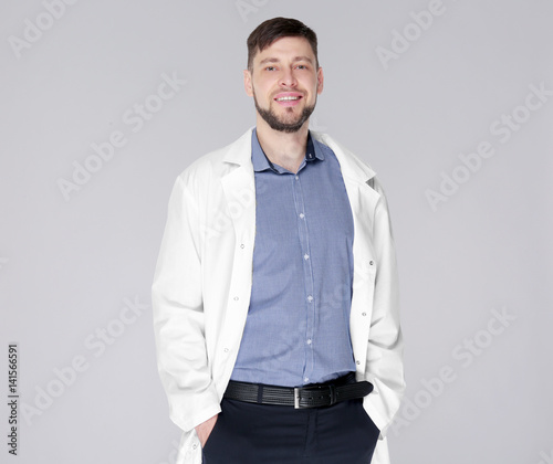 Young handsome pharmacist standing on grey background