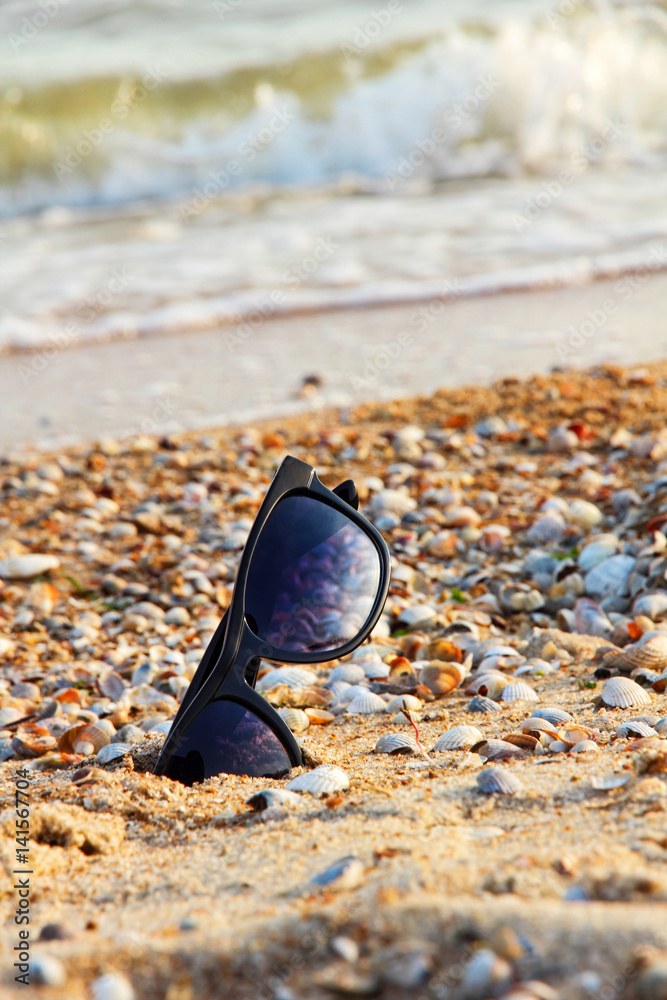 Sunglasses with black frame on sandy beach near surf. Sunglasses with black frame on sandy beach near surf.