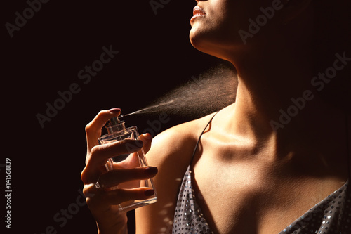 Beautiful young woman with bottle of perfume on dark background photo