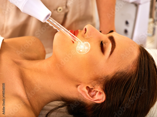 High frequency machine in spa salon. Young woman receiving electric darsonval facial massage after procedure at beauty room close up. photo