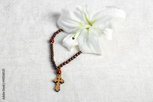 White lily and rosary on light fabric background