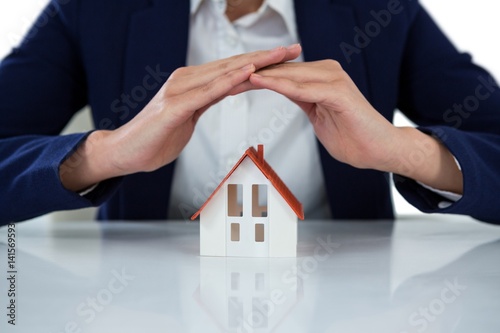 Businesswoman protecting house model with hands