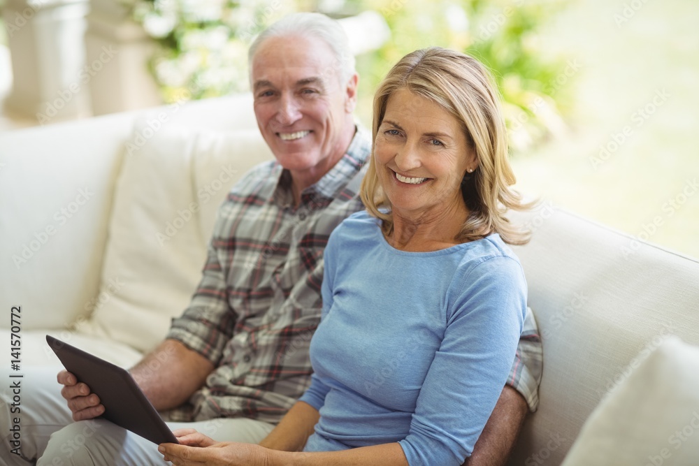 Smiling senior couple sitting on sofa with digital tablet in living room Smiling senior couple sitting on sofa with digital tablet in living room