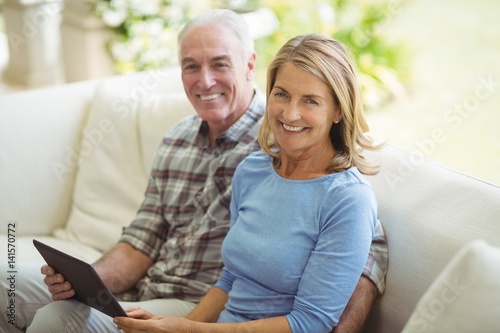 Smiling senior couple sitting on sofa with digital tablet in living room