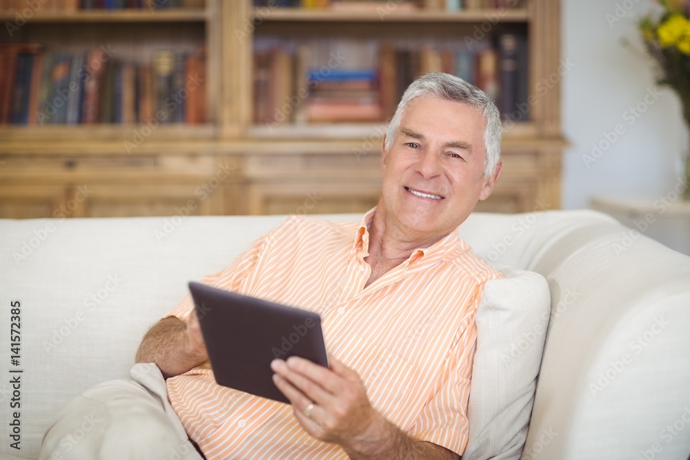 Smiling senior man using digital tablet in living room Smiling senior man using digital tablet in living room