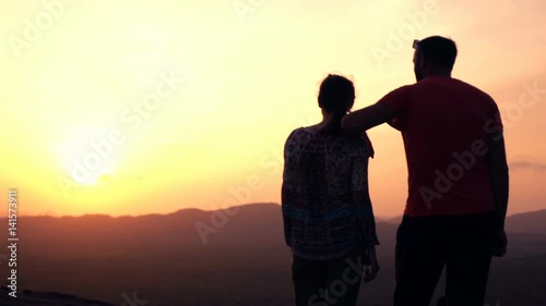 Silhouette of couple admire sunset and landscape standing on hill
