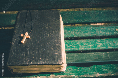 Vintage old holy bible book, grunge textured cover with wooden christian cross. Retro styled image on wood background.