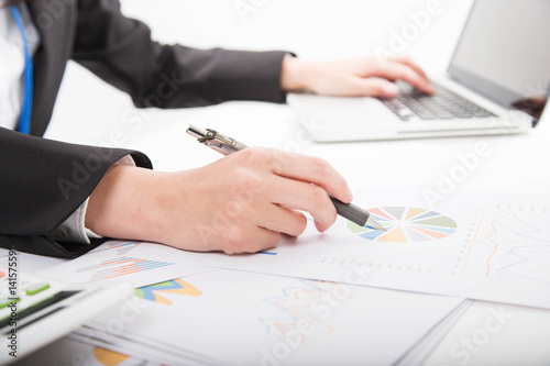 Side view and close up of woman's hands using laptop and writing on business document