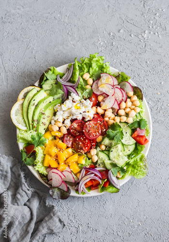 Spring vegetable buddha bowl. Salad with veggies, chickpeas, avocado and feta. Delicious healthy food.  On a gray background, top view
