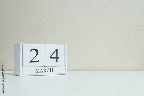 Closeup white wooden calendar with black 24 march word on blurred white wood desk and cream color wallpaper in room textured background with copy space , selective focus at the calendar