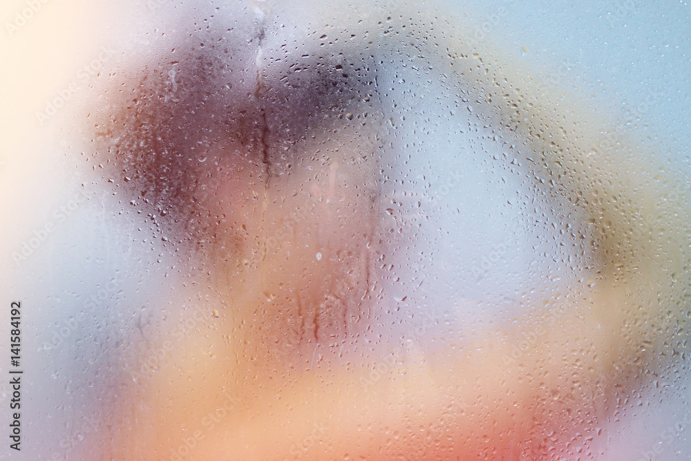 Beautiful young woman washes in the shower behind the misted glass in sunlights