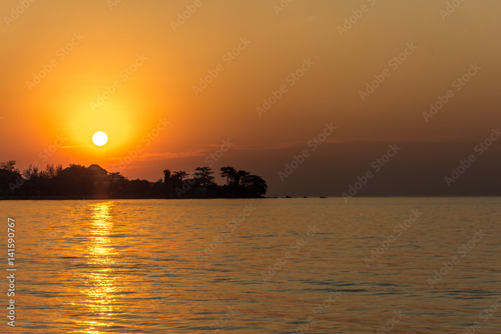 A dramatic golden sunset with the sun just about to set behind a tree lined head land. A dramatic golden sunset with the sun just about to set behind a tree lined head land.