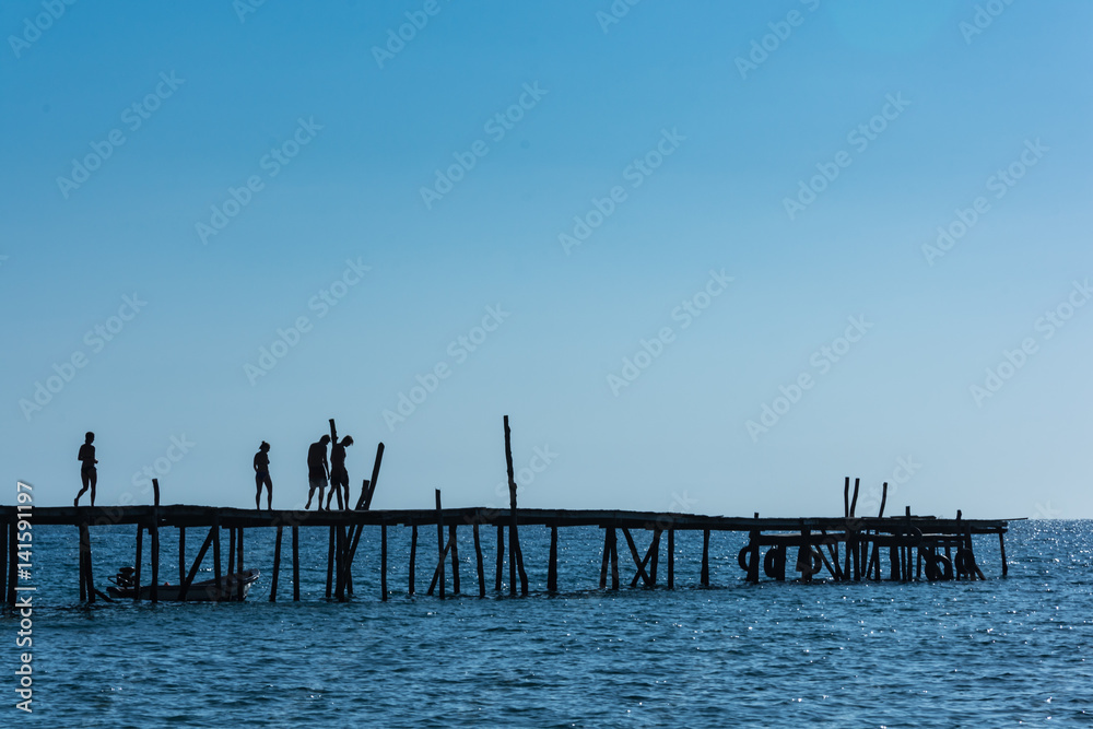 A silhouetted group of friends walk along an old wooden pier