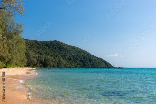 White sandy beach bay with wooden pier and forested headland in the distance on a tropical island.