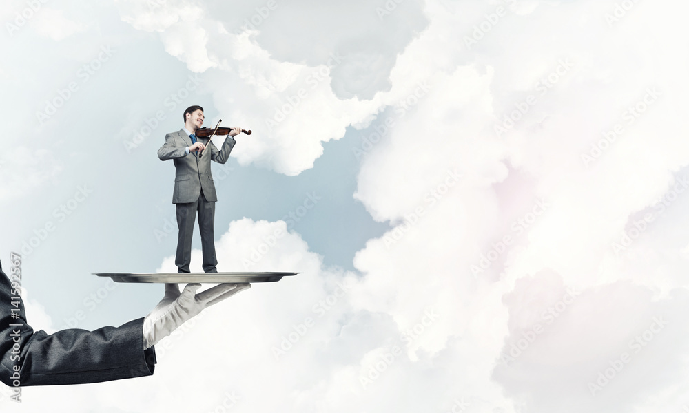 Businessman on metal tray playing violin against blue sky background Businessman on metal tray playing violin against blue sky background