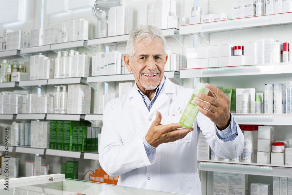 Confident Pharmacist Smiling While Holding Product In Pharmacy Confident Pharmacist Smiling While Holding Product In Pharmacy