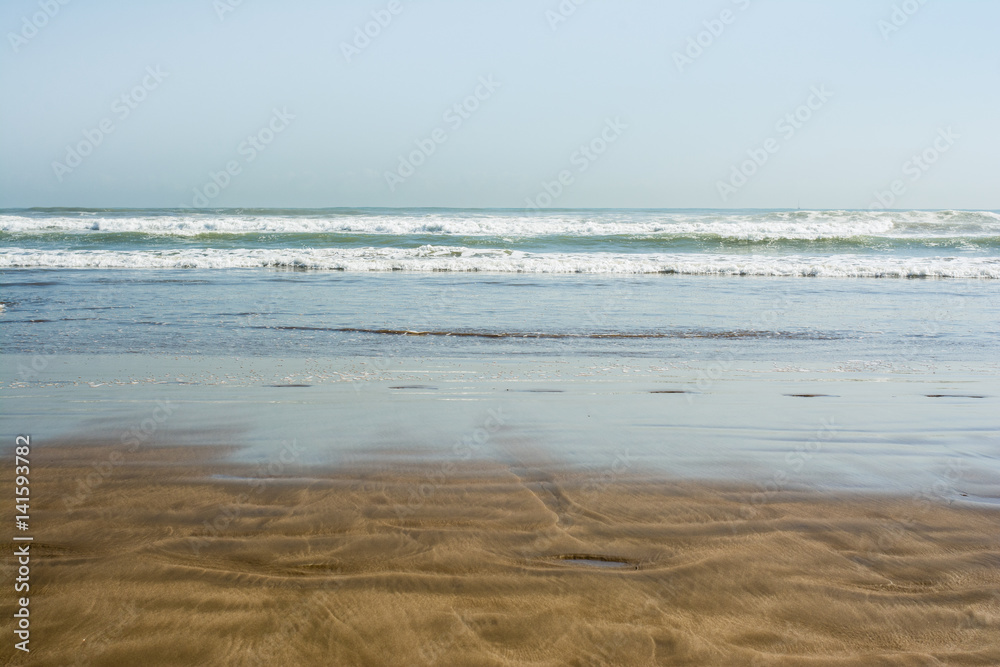 Sea tidal waves with white foam on a sunny sandy beach in resort on summer vacation. Background of ocean water texture