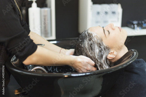 Beautiful young woman with hairdresser washing head at hair salon