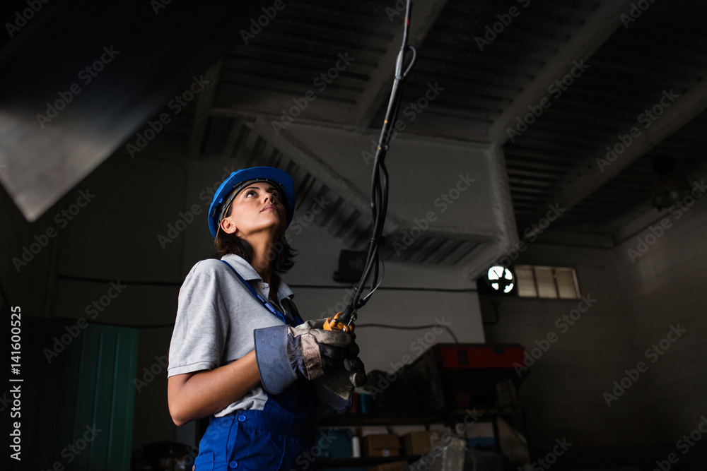 Female mechanic operating a hoist to lift a compressor engine Female mechanic operating a hoist to lift a compressor engine