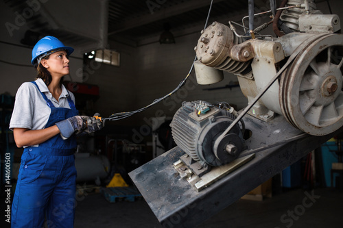 Female mechanic operating a hoist to lift a compressor engine