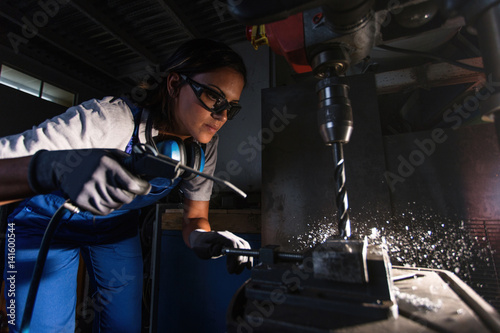 female mechanic using an air blow gun to clean shavings from a column type drill photo