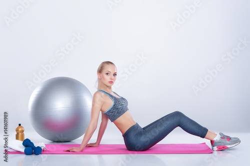 beautiful blonde girl in sportswear does exercises on fitness Mat on gray background
