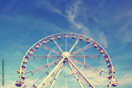 Vintage stylized picture of a Ferris wheel against blue sky.
