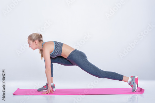 beautiful blonde woman does exercises on fitness Mat on gray background. stretching