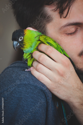young man cuddle his pet parrot on shoulder