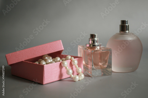 Perfume bottles and pink box with pearl beads on a gray background