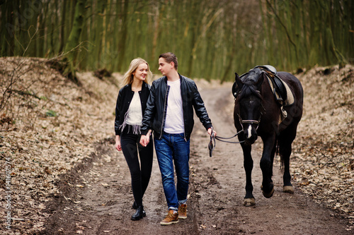 Young stylish couple in love walking with horse at autumn forest.