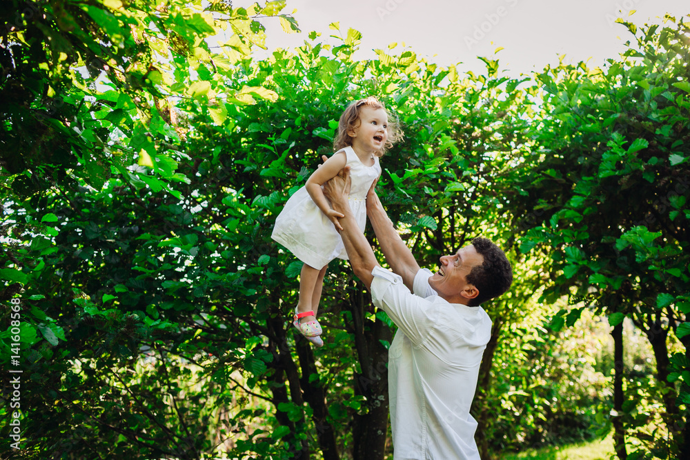 Happy father holds up his little daughter standing in green park Happy father holds up his little daughter standing in green park