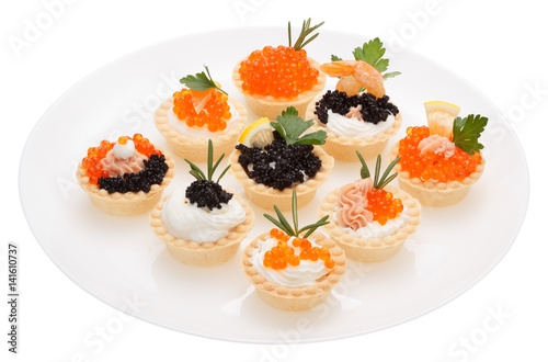 Set tartlets on a white plate. The tartlets filling of mascarpone, smoked salmon. Decorated with red and black caviar, shrimp, lemon and fresh parsley and rosemary.