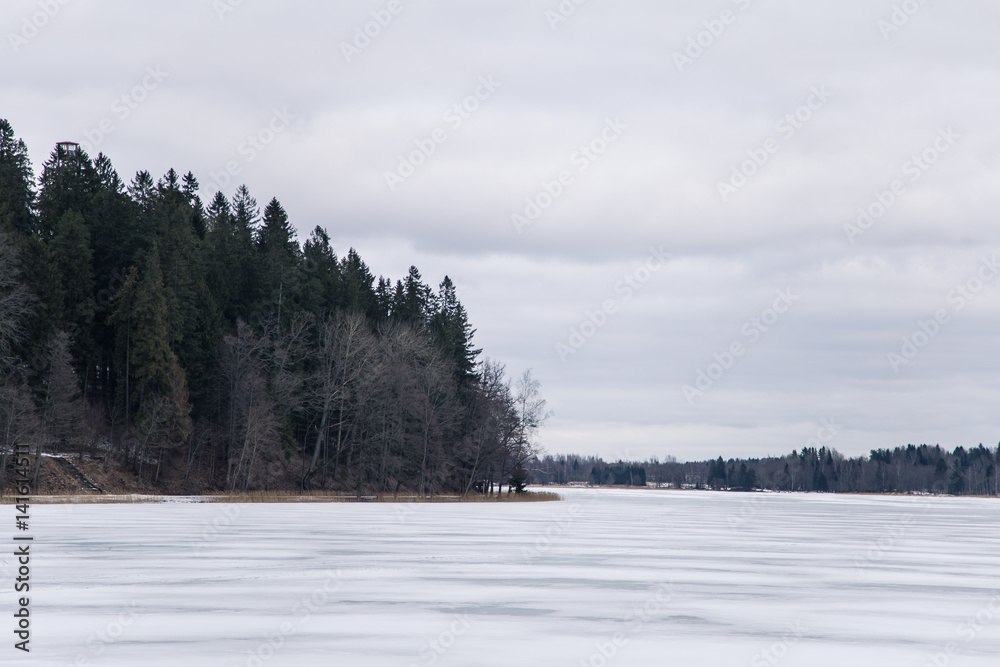 A peaceful winter landscape with a frozen lake in overcast day A peaceful winter landscape with a frozen lake in overcast day