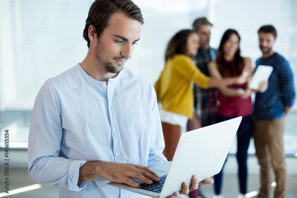 Man using laptop while colleagues discussing in background Man using laptop while colleagues discussing in background
