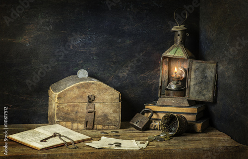 Classic still life with old savings box placed with vintage lamp old books.coins  key and lock on rustic wooden background..