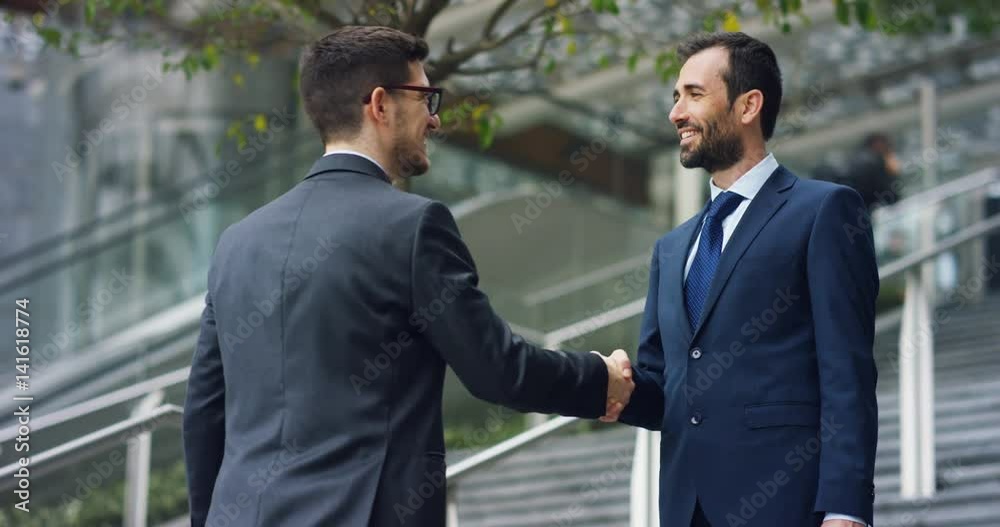 In the city two businessman they shake hands and smile before starting to collaborate on a project. Concept: teamwork, business, contract, bank. In the city two businessman they shake hands and smile before starting to collaborate on a project. Concept: teamwork, business, contract, bank.