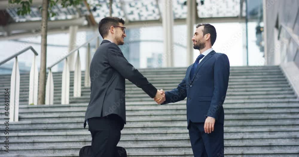 In the city two businessman they shake hands and smile before starting to collaborate on a project. Concept: teamwork, business, contract, bank. In the city two businessman they shake hands and smile before starting to collaborate on a project. Concept: teamwork, business, contract, bank.