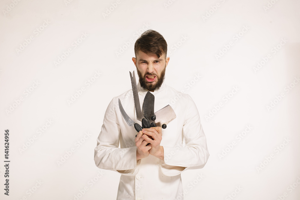 Studio shot of a happy bearded young chef holding sharp knives over white background. Chef with knife. Handsome angry serious cheef holding many sharp knives isolated against white background. Studio shot of a happy bearded young chef holding sharp knives over white background. Chef with knife. Handsome angry serious cheef holding many sharp knives isolated against white background.