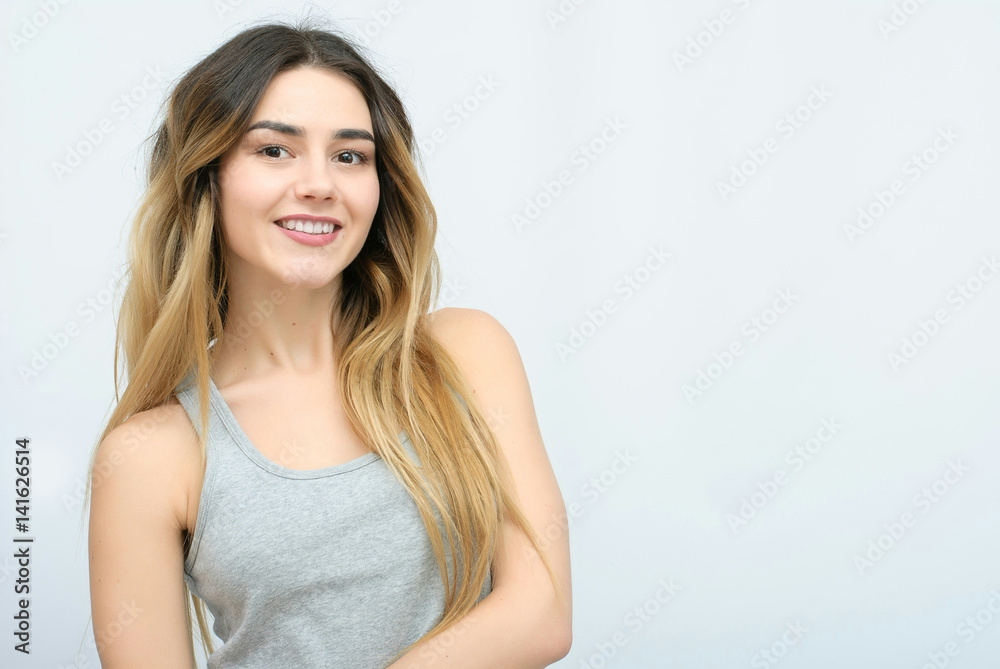 Young girl with long curly hair posing on blue background in studio. She wears shorts, pink T-shirt, pink sunglasses. She keeps hat overhead, holds blue skateboard on booty, looks excited. Young girl with long curly hair posing on blue background in studio. She wears shorts, pink T-shirt, pink sunglasses. She keeps hat overhead, holds blue skateboard on booty, looks excited.